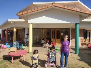 Foto de Mónica, con camiseta morada de Embarrados, y dos niños del Hogar ante la puerta principal